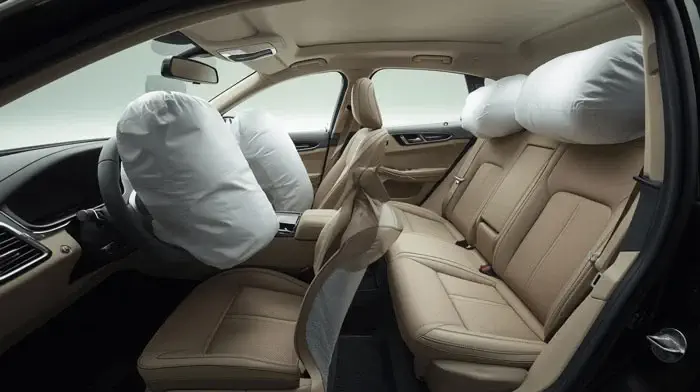Vue de l'intérieur d'une voiture avec des airbags déployés, montrant les sièges avant et arrière en beige.